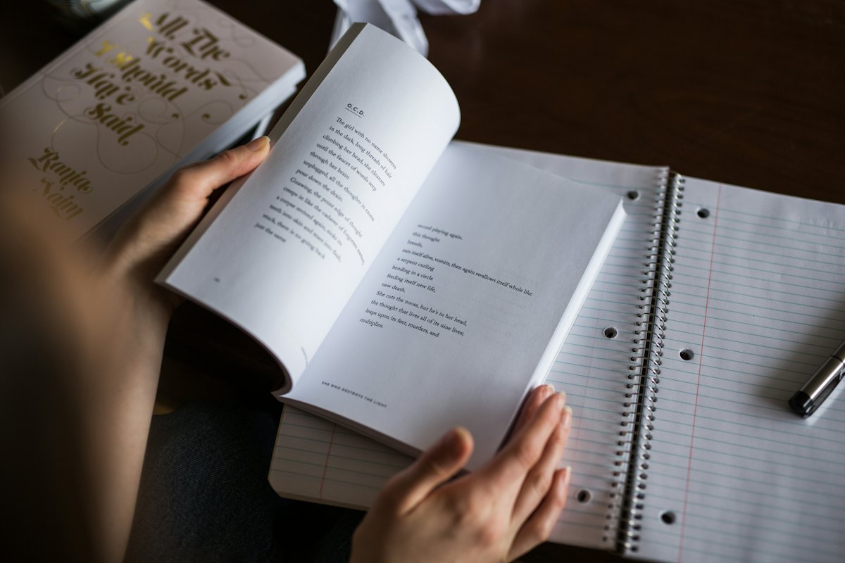 Hands turning the pages of a book next to a notebook